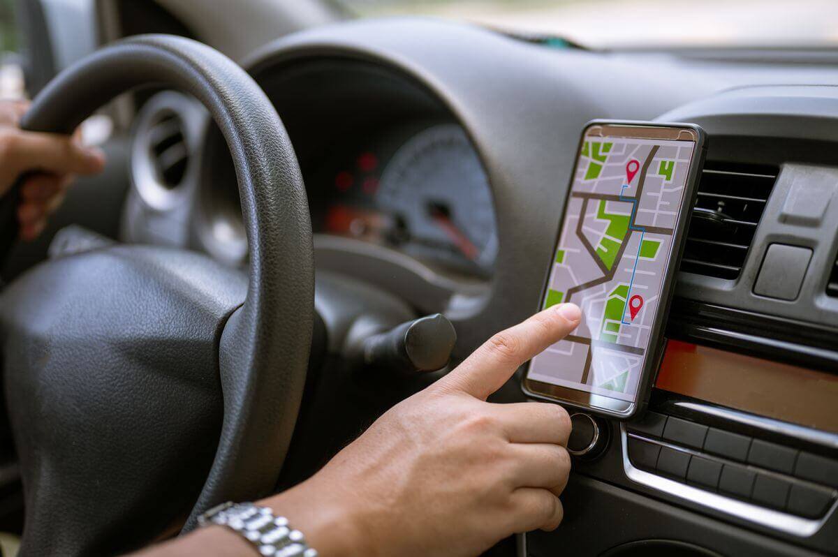 Close-up of a person's hand using a smartphone with a map application attached to the dashboard of a car, symbolizing real-time navigation assistance while driving.